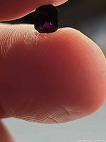 Octagon-cut spinel held between fingers showing deep burgundy-purple hue and facet sharpness