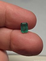 Emerald held between fingertips displaying face of stone