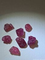 Seven deep pink-red rough spinel crystals on light background