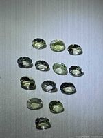 Array of 15 faceted lemon-lime tanzanite stones under direct light