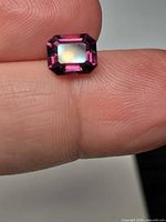 Emerald-cut pink-purple spinel resting on fingertip, table facet up