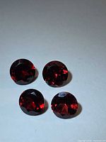 Four round cherry red garnets under direct light showing faceting