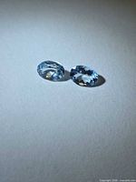 Two oval faceted light blue aquamarines on neutral background