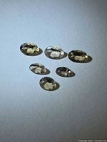 Six champagne colored oval faceted gemstones displayed on neutral background
