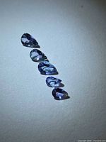 Five pear-cut Tanzanite gemstones arranged in a line on white background
