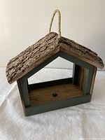 Front angle of wooden bird feeder showing open front, bark roof, green framing