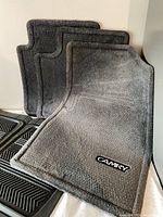 Three grey Toyota Camry carpet mats beside black rubber mats