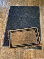 Black ribbed synthetic mat and brown coir mat displayed on wooden floor