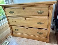 Front view showing three drawers, brass hardware, keyholes, misaligned drawers