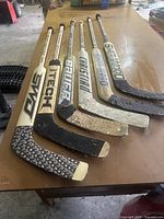 Six goalie sticks laid out to show full length and paddle graphics