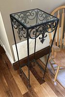 Full view of metal plant stand showing glass top and scrollwork sides