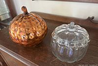 Amber glass pumpkin and clear glass lidded pumpkin jar on wooden surface