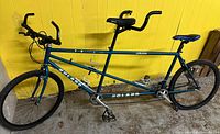 Full view of teal Roland tandem bicycle against wall