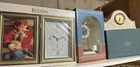 All three boxed clocks on shelf: Bulova photo frame clock, Thomas Kinkade anniversary clock, Lenox mantel clock