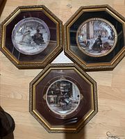 Three framed octagonal plates showing winter and interior scenes