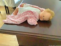 Doll lying on table, full view showing vinyl head, cloth body, pink polka-dot robe