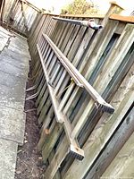 Full view of aluminum ladder leaning against fence