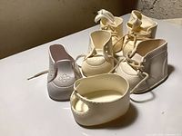 Front and angled view showing six assorted ivory vinyl doll shoes with lace-up, oxford and slip-on styles