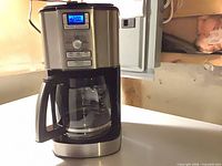 Front view of Cuisinart coffee maker showing stainless steel panel, blue LCD display lit, and attached glass carafe