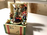 Open music box showing Christmas scene with soldier, tree, train, teddy bear and toys
