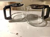 Two glass KitchenAid coffee carafes side by side showing overall form, lids, handles, glass clarity and measurement markings