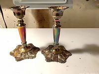 Front view of both candlesticks upright showing patina and ornate bases