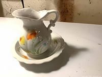 Pitcher on saucer, front view shows floral design and scroll handle