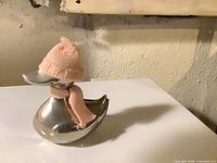 Front and side view of polished silver duck wearing pink knit hat and scarf