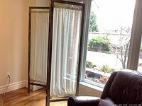 Full view of divider angled near window showing two sheer fabric panels and wood frame