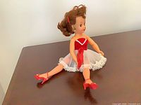 Front view of doll seated showing dress, shoes, earrings