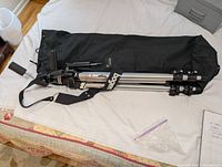 Folded Bogen 3021 tripod placed on black carrying bag with shoulder strap visible