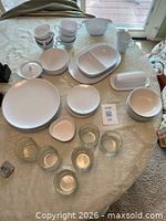 Full assortment of white plastic dinnerware and six glass tumblers arranged on table