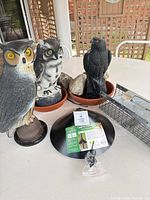 Group shot showing two owl statues, crow statue, squirrel baffle with packaging, Havahart trap
