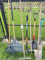 All eight long-handled garden tools leaned against fence for full view