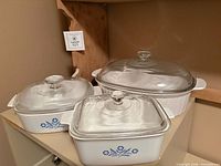 Three casserole dishes with lids displayed together on shelf