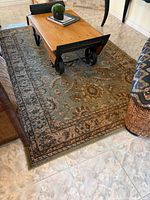 Full view of the rectangular green and beige patterned area rug on tile floor beneath a coffee table