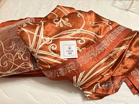 Overall view of folded orange-rust silk bedding pieces showing scroll embroidery and sealed pillow shams