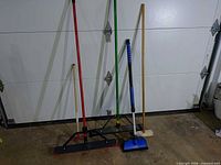 All five brooms and brushes standing against garage door