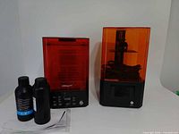 Two Creality machines side by side with resin bottles and papers