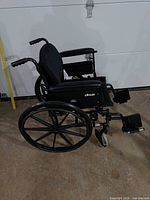 Left side view of wheelchair showing frame, rear wheel, footrests