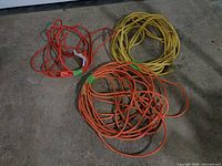 Three coiled extension cords: two orange, one yellow