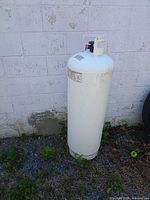 Full view of tall white propane cylinder against wall