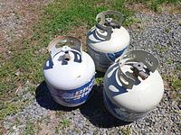 Three propane cylinders standing on gravel, view of tops and labels