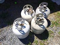 Four propane tanks grouped outdoors on gravel