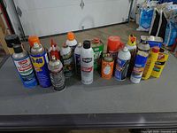 Row of approx. 15 assorted automotive chemical containers on a table
