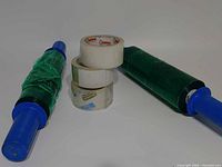 Two green stretch wrap rolls with blue handles and three clear tape rolls