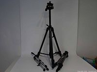 All three tripods displayed; tall black tripod standing, two silver tripods folded on floor