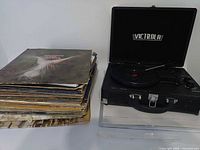Victrola suitcase turntable alongside stack of vinyl records