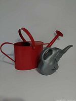 Red metal watering can and grey elephant watering can side by side