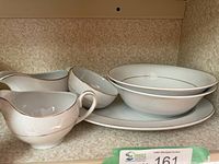 Group view of six white ironstone serving pieces with gold trim on shelf
